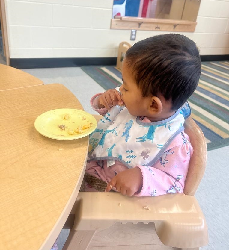 A young girl in a PLASP Early Learning and Child Care Centre sits at a table and eats a healthy snack